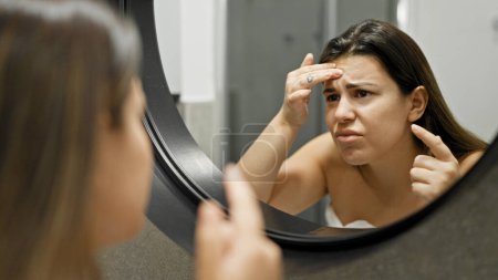 Photo for Young beautiful hispanic woman looking for pimples at the mirror in the bathroom - Royalty Free Image