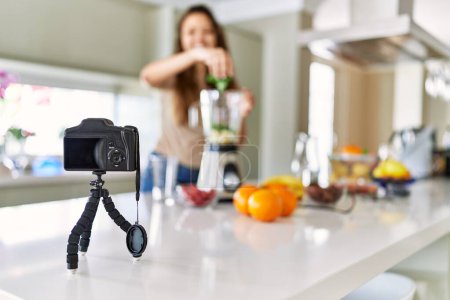 Foto de Joven hermosa mujer hispana preparando batido de verduras con licuadora grabación video tutorial con cámara en la cocina - Imagen libre de derechos