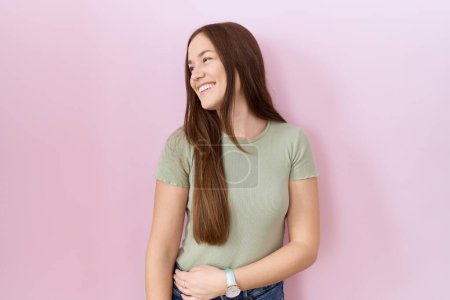 Photo for Beautiful brunette woman standing over pink background looking away to side with smile on face, natural expression. laughing confident. - Royalty Free Image