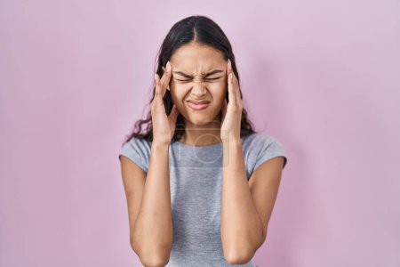 Photo for Young brazilian woman wearing casual t shirt over pink background with hand on head for pain in head because stress. suffering migraine. - Royalty Free Image