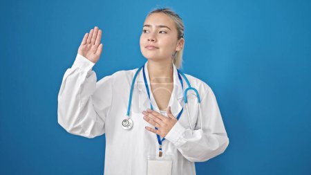 Téléchargez les photos : Jeune belle femme hispanique médecin faire un serment avec la main sur la poitrine sur fond bleu isolé - en image libre de droit