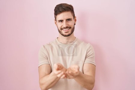 Photo for Hispanic man with beard standing over pink background smiling with hands palms together receiving or giving gesture. hold and protection - Royalty Free Image