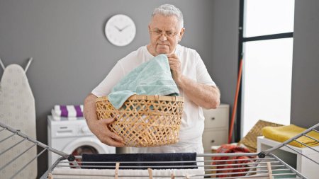 Photo for Middle age grey-haired man holding basket smelling clean clothes at laundry room - Royalty Free Image