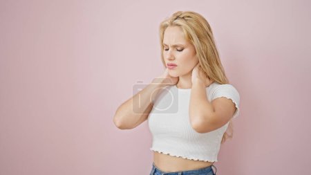 Foto de Mujer rubia joven que sufre de dolor cervical sobre fondo rosa aislado - Imagen libre de derechos