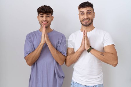 Photo for Homosexual gay couple standing over white background praying with hands together asking for forgiveness smiling confident. - Royalty Free Image