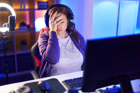 Foto de Joven hermosa mujer de tamaño grande streamer estresado utilizando la computadora en la sala de juegos - Imagen libre de derechos