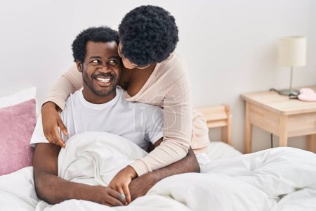 Téléchargez les photos : Africain américain homme et femme couple étreignant l'autre assis sur le lit à chambre - en image libre de droit