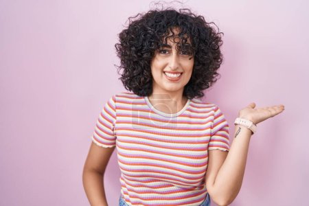 Téléchargez les photos : Jeune femme du Moyen-Orient debout sur fond rose souriant joyeuse présentation et pointant avec la paume de la main en regardant la caméra. - en image libre de droit