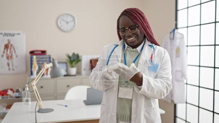 Foto de Mujer africana con médico de pelo trenzado poniendo guantes para la seguridad en la clínica - Imagen libre de derechos