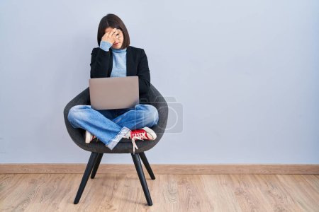 Foto de Mujer hispana joven sentada en silla usando computadora portátil cansada frotando nariz y ojos sintiendo fatiga y dolor de cabeza. concepto de estrés y frustración. - Imagen libre de derechos