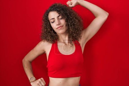 Photo for Hispanic woman with curly hair standing over red background stretching back, tired and relaxed, sleepy and yawning for early morning - Royalty Free Image