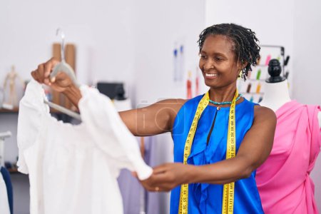 Téléchargez les photos : Middle age african american woman tailor smiling confident holding t shirt at atelier - en image libre de droit