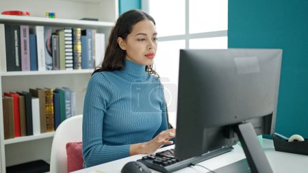 Téléchargez les photos : Jeune belle étudiante hispanique utilisant un ordinateur dans une salle de classe universitaire - en image libre de droit