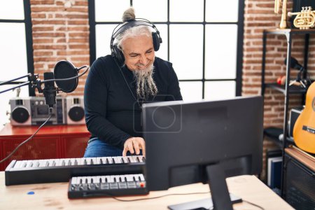 Foto de Hombre músico de pelo gris de mediana edad sonriendo confiado tocando el piano en el estudio de música - Imagen libre de derechos