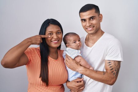 Photo for Young hispanic couple with baby standing together over isolated background pointing with hand finger to face and nose, smiling cheerful. beauty concept - Royalty Free Image