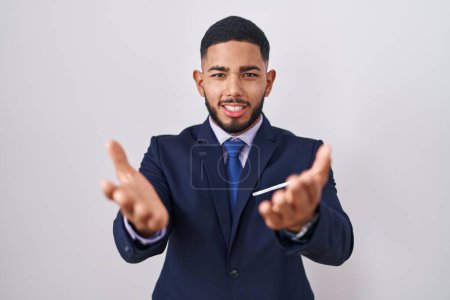 Photo for Young hispanic man wearing business suit and tie smiling cheerful offering hands giving assistance and acceptance. - Royalty Free Image