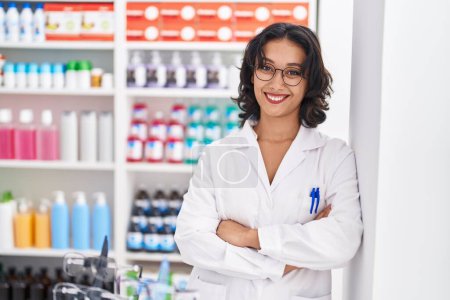Foto de Young beautiful hispanic woman pharmacist smiling confident standing with arms crossed gesture at pharmacy - Imagen libre de derechos