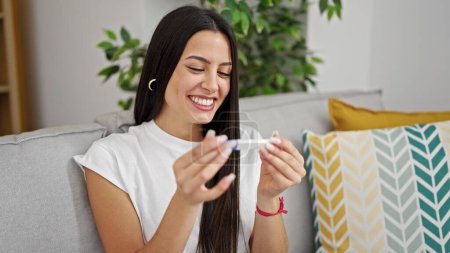 Téléchargez les photos : Jeune belle femme hispanique souriant confiant tenant test de grossesse à la maison - en image libre de droit