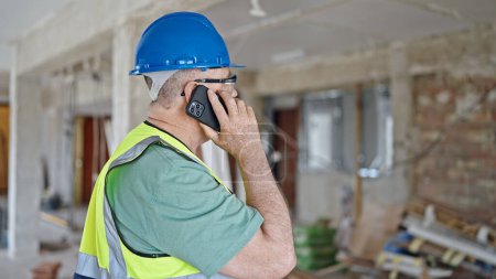 Photo for Middle age grey-haired man builder talking on smartphone with relaxed expression at construction site - Royalty Free Image
