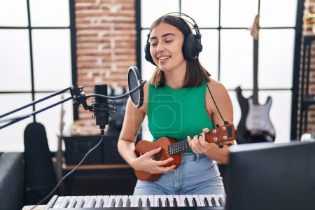 Téléchargez les photos : Jeune musicienne hispanique chantant une chanson jouant ukelele au studio de musique - en image libre de droit