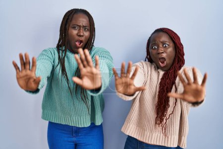 Photo for Two african woman standing over blue background doing stop gesture with hands palms, angry and frustration expression - Royalty Free Image