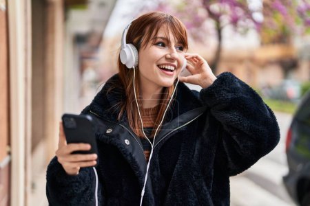 Foto de Mujer joven sonriendo confiada escuchando música en la calle - Imagen libre de derechos