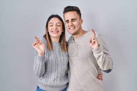 Téléchargez les photos : Jeune couple hispanique debout sur fond blanc geste doigt croisé souriant avec espoir et les yeux fermés. chance et concept superstitieux. - en image libre de droit