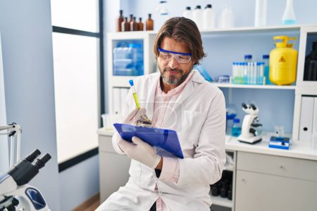 Photo for Middle age man scientist holding test tube reading document at laboratory - Royalty Free Image