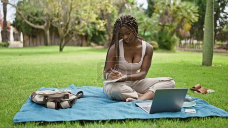 Foto de Estudiante afroamericana usando laptop tomando notas en la universidad del campus - Imagen libre de derechos