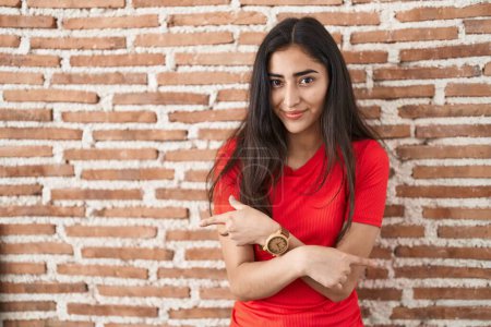 Photo for Young teenager girl standing over bricks wall pointing to both sides with fingers, different direction disagree - Royalty Free Image