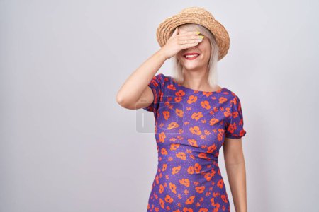 Photo for Young caucasian woman wearing flowers dress and summer hat smiling and laughing with hand on face covering eyes for surprise. blind concept. - Royalty Free Image