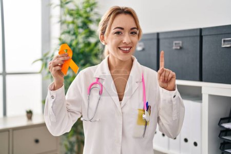 Photo for Hispanic doctor woman holding awareness orange ribbon surprised with an idea or question pointing finger with happy face, number one - Royalty Free Image