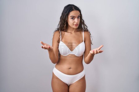 Photo for Young hispanic woman wearing white lingerie clueless and confused with open arms, no idea concept. - Royalty Free Image