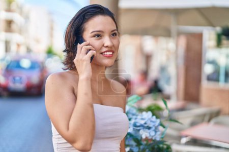 Téléchargez les photos : Jeune femme hispanique souriant confiant parler sur le smartphone à la terrasse du café - en image libre de droit