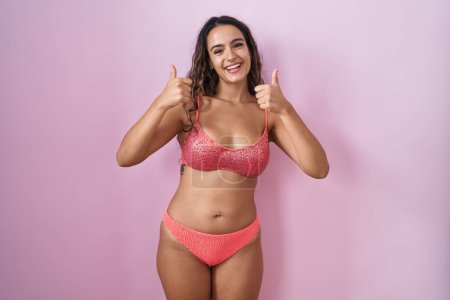 Photo for Young hispanic woman wearing lingerie over pink background success sign doing positive gesture with hand, thumbs up smiling and happy. cheerful expression and winner gesture. - Royalty Free Image