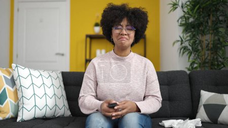 Foto de Joven afroamericana mujer viendo tv sentado en sofá en casa - Imagen libre de derechos