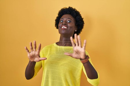 Photo for African young woman standing over yellow studio afraid and terrified with fear expression stop gesture with hands, shouting in shock. panic concept. - Royalty Free Image