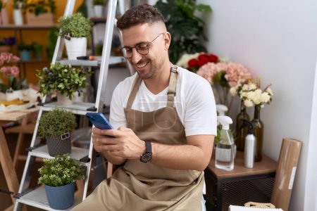 Photo for Young hispanic man florist smiling confident using smartphone at flower shop - Royalty Free Image