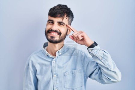 Photo for Young hispanic man with beard standing over blue background smiling pointing to head with one finger, great idea or thought, good memory - Royalty Free Image