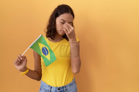 Photo for Young hispanic woman holding brazil flag tired rubbing nose and eyes feeling fatigue and headache. stress and frustration concept. - Royalty Free Image