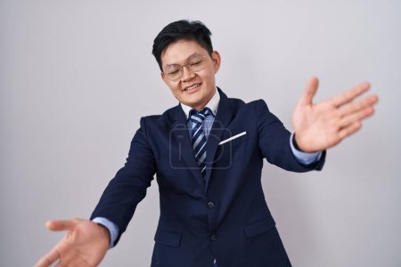 Photo for Young asian man wearing business suit and tie looking at the camera smiling with open arms for hug. cheerful expression embracing happiness. - Royalty Free Image