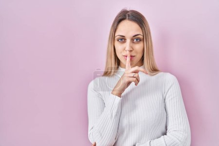 Photo for Young blonde woman wearing white sweater over pink background asking to be quiet with finger on lips. silence and secret concept. - Royalty Free Image