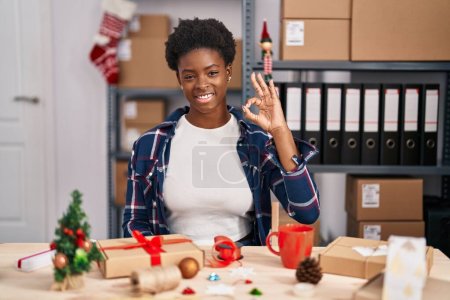 Téléchargez les photos : Femme afro-américaine travaillant dans une petite entreprise faisant décoration de Noël souriant positif faire ok signe avec la main et les doigts. expression réussie. - en image libre de droit