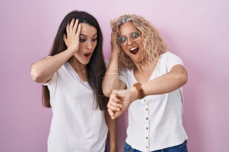 Téléchargez les photos : Mère et fille debout ensemble sur fond rose regardant le temps de la montre inquiet, peur de se faire tard - en image libre de droit