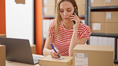 Téléchargez les photos : Jeune femme blonde ecommerce travailleur d'affaires parlant sur smartphone écriture sur paquet au bureau - en image libre de droit