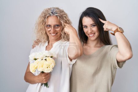 Foto de Madre e hija sosteniendo ramo de flores blancas sonriendo señalando a la cabeza con un dedo, gran idea o pensamiento, buena memoria - Imagen libre de derechos