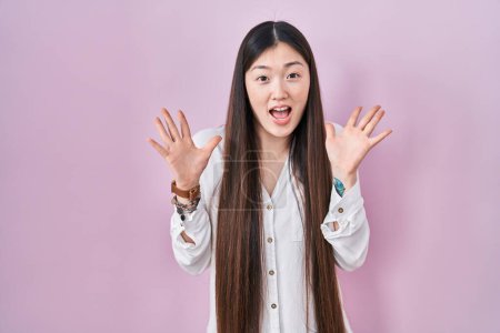 Téléchargez les photos : Jeune femme chinoise debout sur fond rose célébrant fou et étonné pour le succès avec les bras levés et les yeux ouverts hurlant excité. concept gagnant - en image libre de droit