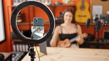 Photo for Young beautiful hispanic woman musician recording video tutorial playing ukulele at music studio - Royalty Free Image