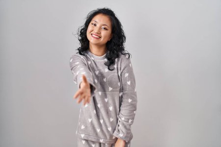Foto de Joven mujer asiática vistiendo pijama sonriente amistoso ofreciendo apretón de manos como saludo y bienvenida. negocios exitosos. - Imagen libre de derechos