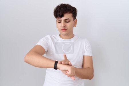 Téléchargez les photos : Jeune homme non binaire portant un t-shirt blanc décontracté vérifiant l'heure sur la montre-bracelet, détendu et confiant - en image libre de droit